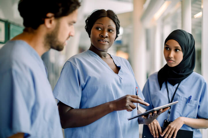 A clinical nurse specialist in a hospital hallway having a discussion with two younger nursing staff members.